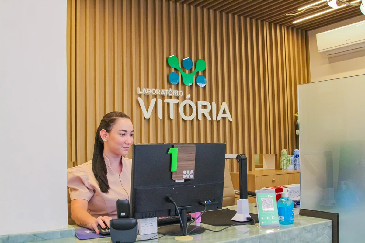 Recepcionista do Laboratório Vitória atendendo no balcão